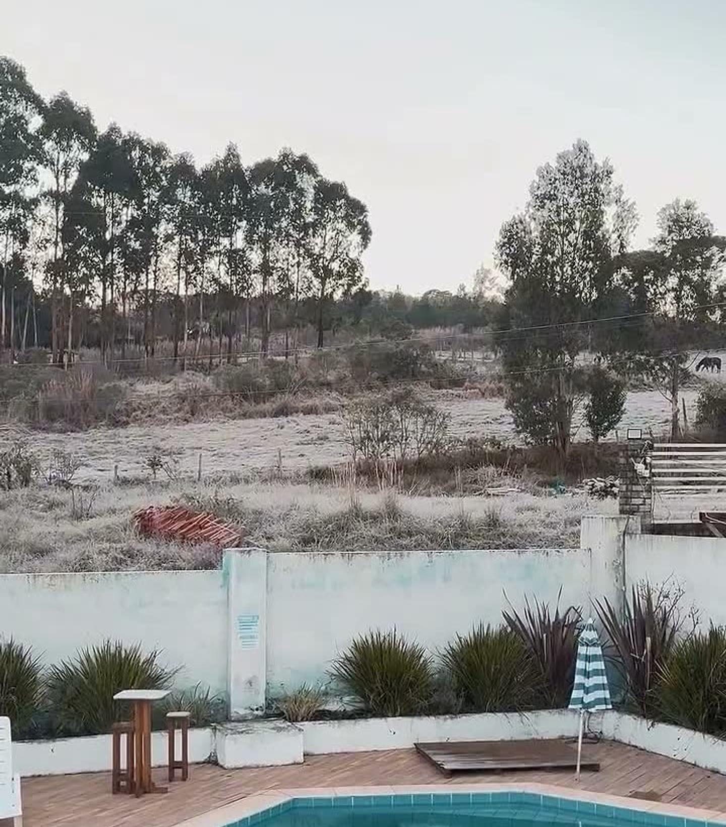 Manhã de geada na pousada, com o campo branco atrás da piscina