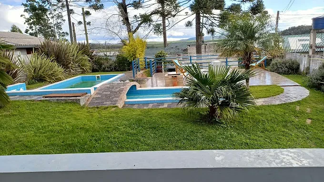 As duas piscinas da pousada, ligadas por um deck de pedra, com o gramado e a serra ao fundo