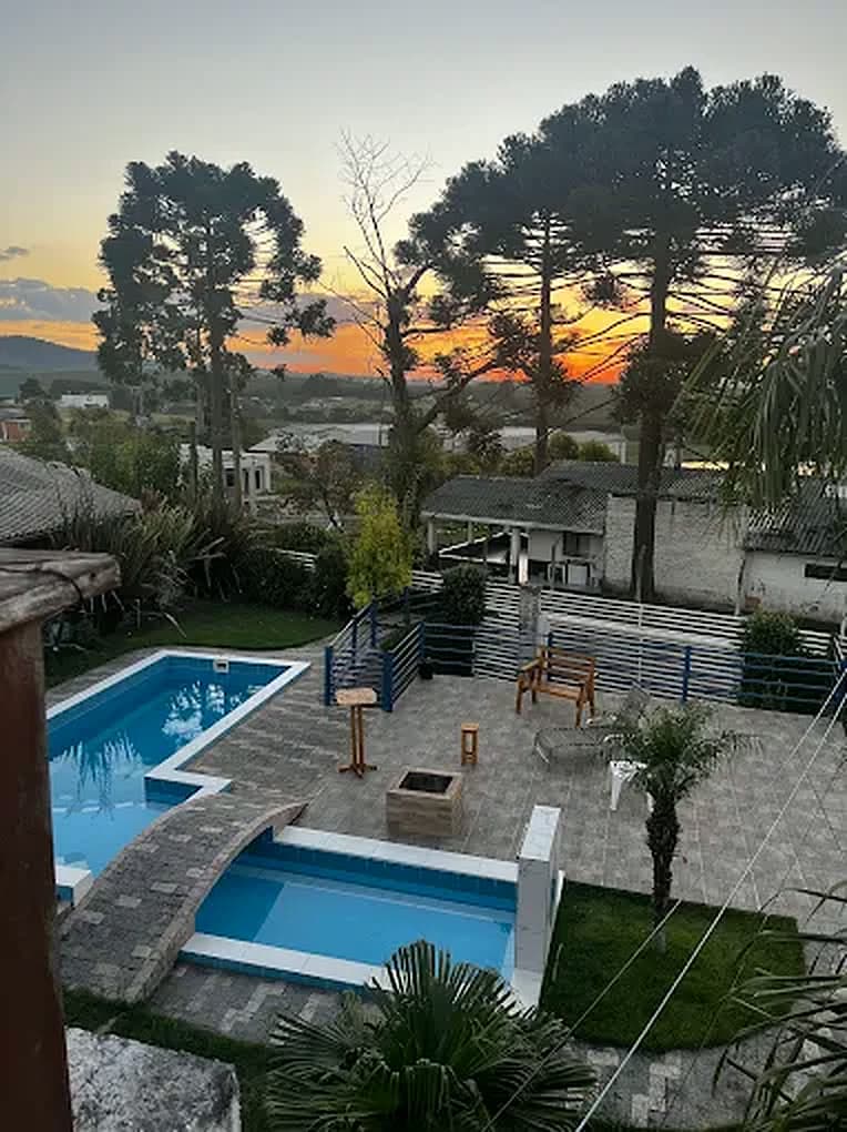 As piscinas ao pôr do sol, com as araucárias recortadas contra o céu alaranjado